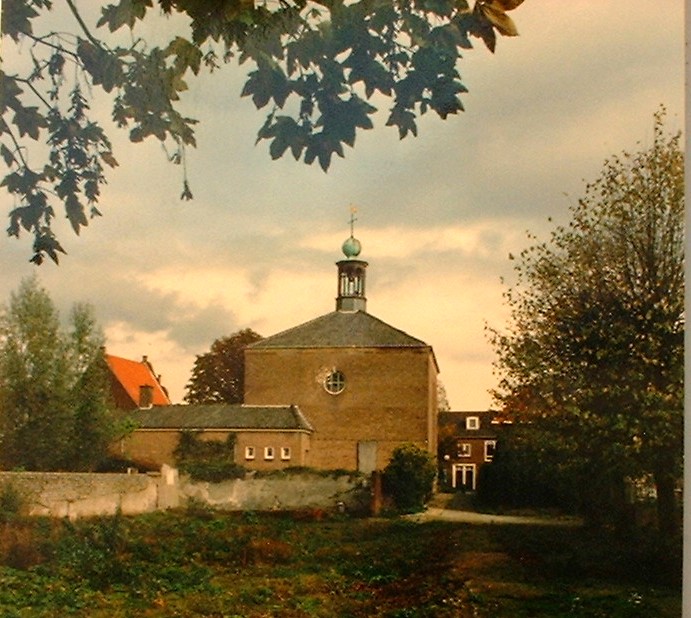 29.B1. Zicht op grijze muur met kerkhofje erachter en de kerk. Ko